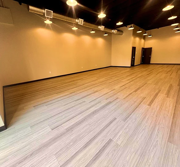 Spacious commercial interior with wood flooring, beige walls, and ceiling-mounted industrial lights.