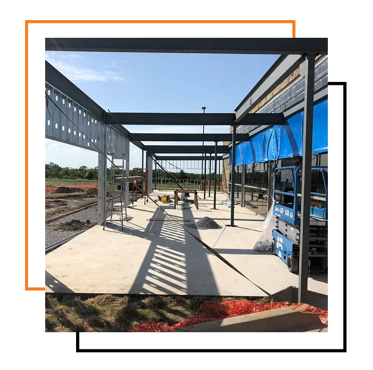 Steel frame structure under construction with beams, scaffolding, and lift equipment on a concrete foundation.